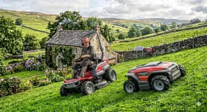 An automatic robotic lawn mower climbing and cutting a damp, sloping lawn in a British back garden.
