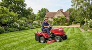 A garden tractor style ride on lawn mower navigating a gentle slope on a British estate.