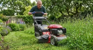 A heavy-duty self-propelled petrol lawn mower efficiently cutting through long, thick grass.