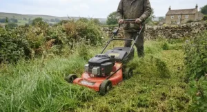 A powerful self-propelled lawn mower tackling long, thick grass in a UK countryside garden.