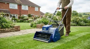 A modern cordless battery-powered cylinder lawn mower being pushed across a suburban garden lawn.